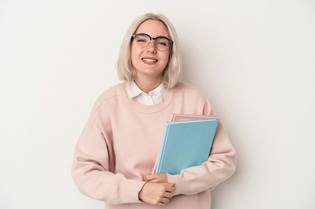 Jeune étudiante caucasienne tenant des livres isolés sur fond blanc en riant et en s'amusant.