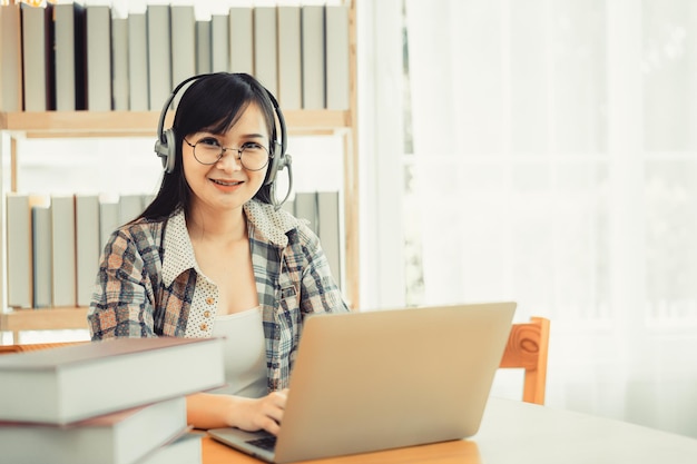Jeune étudiante en chemise à carreaux assise à la table à l'aide d'un ordinateur portable lors de ses études.