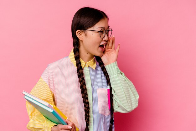 Jeune étudiante Chinoise Tenant Des Livres Portant Une Chemise Et Une Tresse Multicolores à La Mode, Isolée Sur Fond Rose Criant Et Tenant La Paume Près De La Bouche Ouverte.