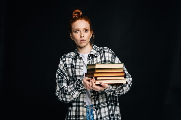 Jeune étudiante choquée tenant des livres et regardant la caméra sur fond noir