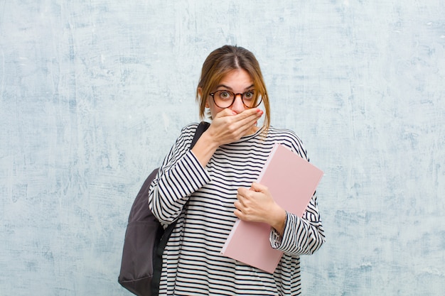 Jeune étudiante couvrant la bouche avec les mains avec une expression choquée et surprise, gardant un secret ou disant: oups