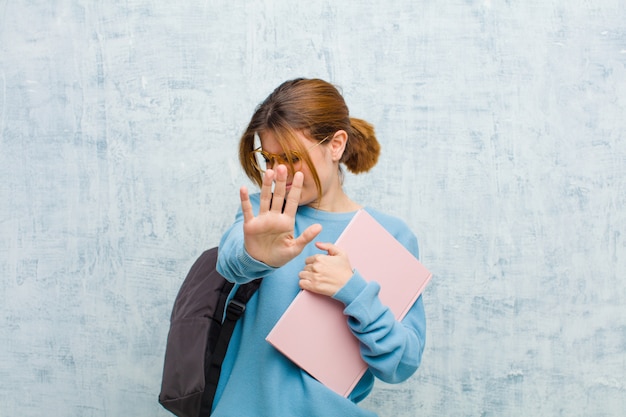 Jeune étudiante couvrant le visage avec la main et mettant l'autre main à l'avant pour arrêter l'appareil photo, refusant les photos ou les images contre le mur de grunge