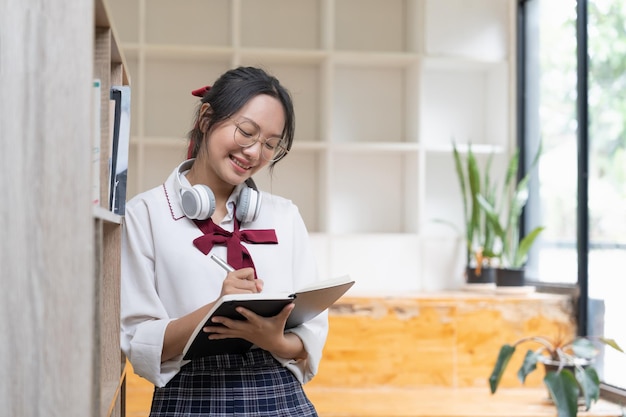 Jeune étudiante faisant des devoirs dans la bibliothèque Femme asiatique prenant des notes à partir de manuels