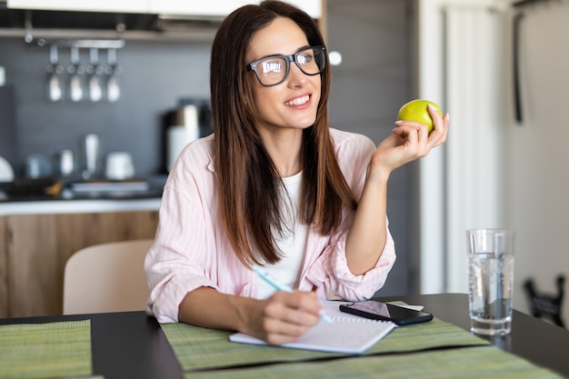 Jeune étudiante faisant ses devoirs à la maison dans la cuisine