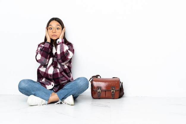 Jeune étudiante femme assise sur le sol frustré et couvrant les oreilles