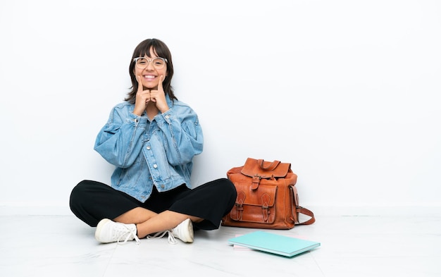 Jeune étudiante femme assise sur le sol isolé sur fond blanc souriant avec une expression heureuse et agréable