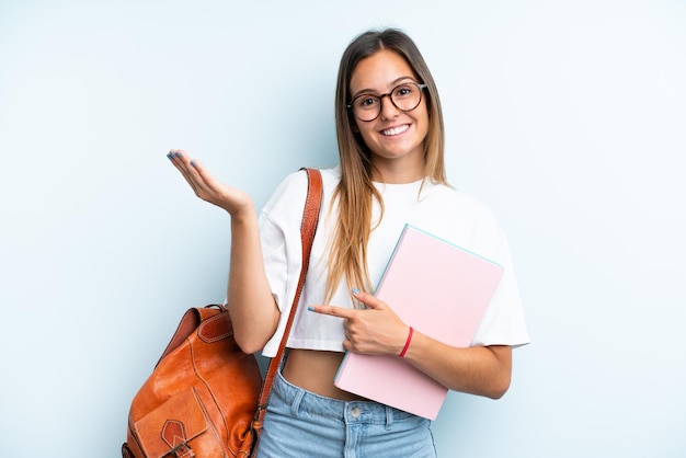 Jeune étudiante femme isolée sur fond bleu tendant les mains sur le côté pour inviter à venir