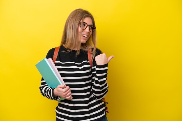 Jeune étudiante femme isolée sur fond jaune pointant vers le côté pour présenter un produit