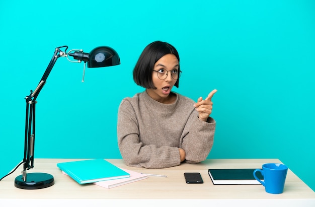 Jeune étudiante femme métisse étudiant sur une table pointant vers l'extérieur