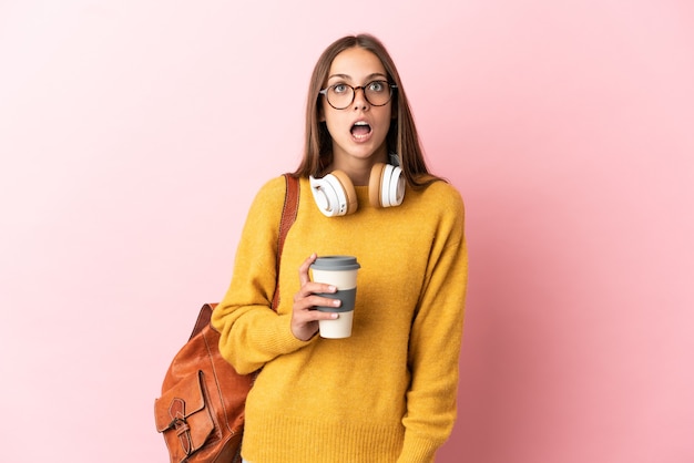 Jeune étudiante sur fond rose isolé à la recherche et avec une expression de surprise