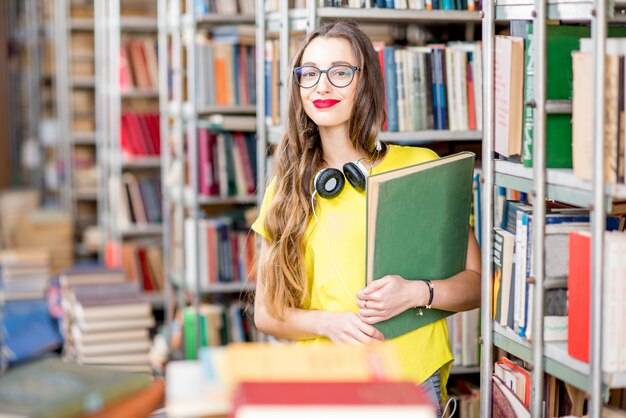 Jeune étudiante heureuse et enthousiaste lisant des livres à l'ancienne bibliothèque