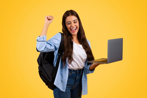 Une jeune étudiante heureuse profite de la bonne nouvelle et célèbre le succès avec un ordinateur portable