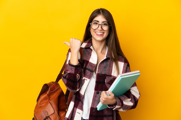 Jeune étudiante isolée sur fond jaune pointant vers le côté pour présenter un produit