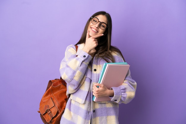 Jeune étudiante isolée sur fond violet heureuse et souriante