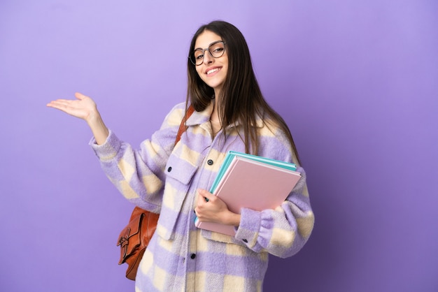 Jeune étudiante isolée sur fond violet tendant les mains sur le côté pour inviter à venir