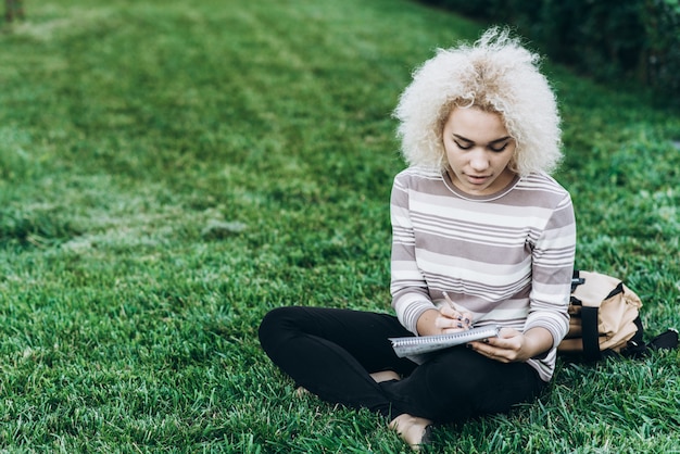 Une jeune étudiante joyeuse s&#39;assoit sur une herbe au campus