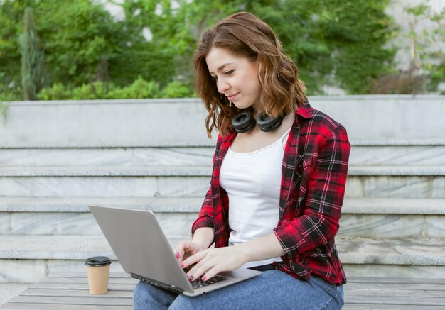 Une jeune étudiante joyeuse utilise un ordinateur portable à l'extérieur. Concept de travail ou d'éducation à distance