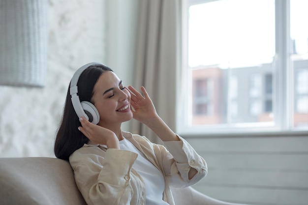 Une jeune étudiante à la maison assise sur un canapé écoute de la musique dans un casque fermé les yeux se repose