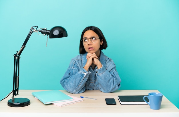 Jeune étudiante métisse femme étudiant sur une table ayant des doutes et avec une expression de visage confuse