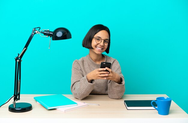 Jeune étudiante métisse femme étudiant sur une table envoyant un message avec le mobile