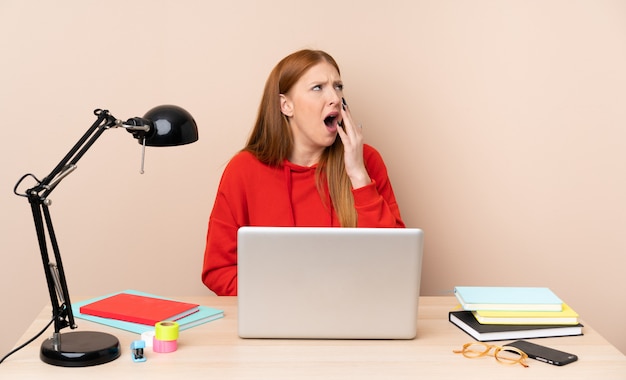 Jeune étudiante en milieu de travail avec un ordinateur portable bâillant et couvrant la bouche grande ouverte avec la main