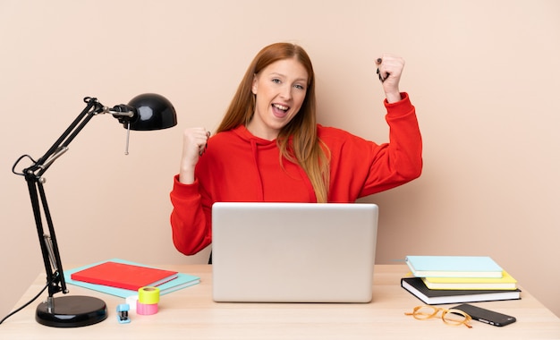 Jeune étudiante en milieu de travail avec un ordinateur portable célébrant une victoire