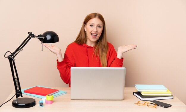 Jeune étudiante en milieu de travail avec un ordinateur portable avec une expression faciale choquée