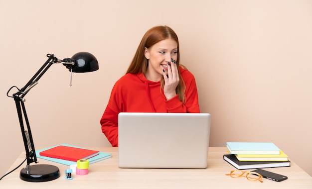 Jeune étudiante en milieu de travail avec un ordinateur portable souriant beaucoup