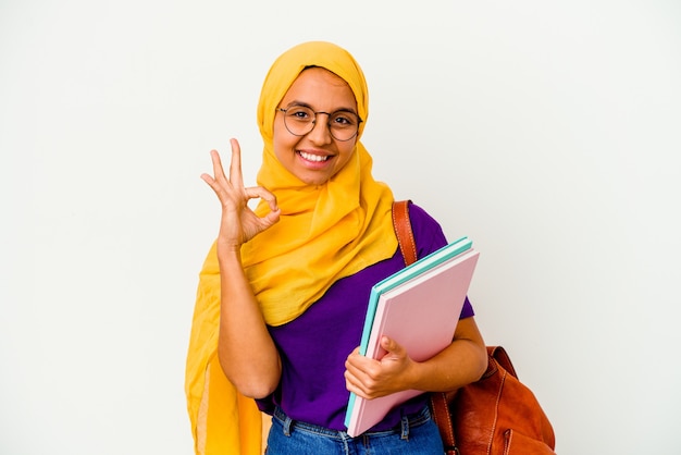 Jeune étudiante musulmane portant un hijab isolé sur fond blanc joyeux et confiant montrant le geste ok.