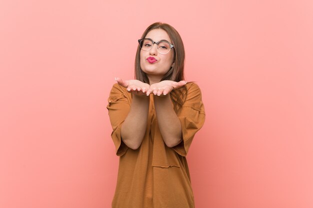 Jeune étudiante portant des lunettes, pliant les lèvres et tenant les paumes pour envoyer l'air