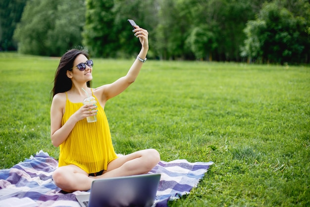 Jeune étudiante prenant un selfie sur smartphone assis sur l&#39;herbe.