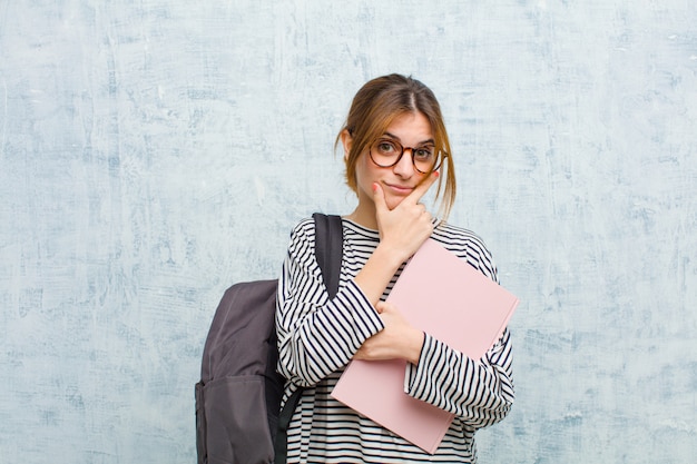 Jeune étudiante à la recherche de sérieux, pensif et méfiant, avec un bras croisé et la main sur le menton, options de pondération sur fond de mur grunge