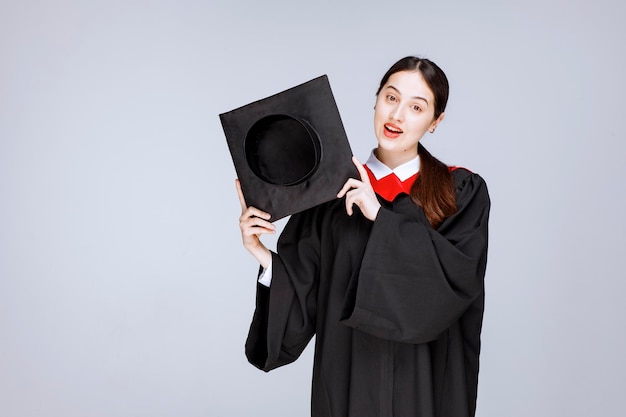 Jeune étudiante en robe montrant sa casquette de graduation. photo de haute qualité