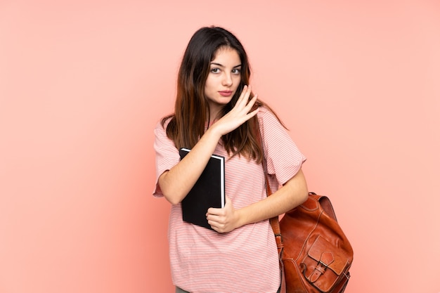 Jeune étudiante se rendant à l'université sur un mur rose isolé chuchotant quelque chose