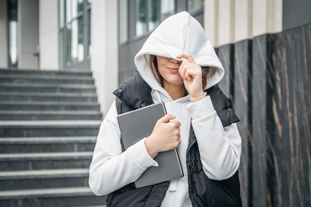 Une jeune étudiante se tient debout avec une tablette numérique dans les mains à l'extérieur