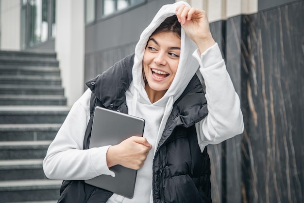 Une jeune étudiante se tient debout avec une tablette numérique dans les mains à l'extérieur