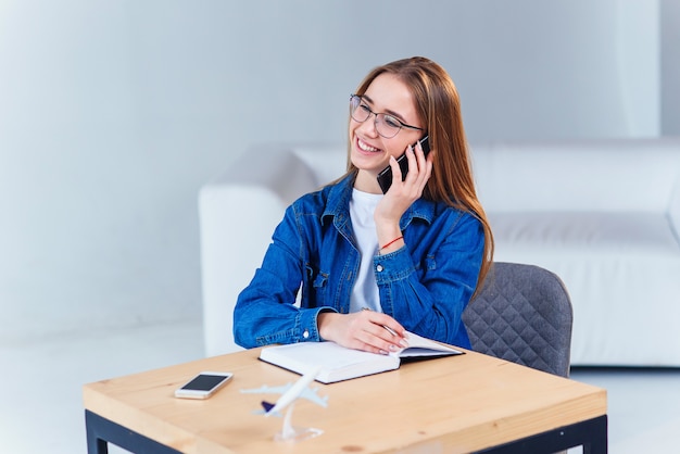 Jeune étudiante séduisante utilise un smartphone tout en étudiant à la maison.