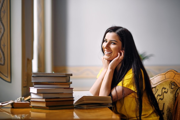 Jeune étudiante souriante et enthousiaste lisant des livres à l'ancienne bibliothèque