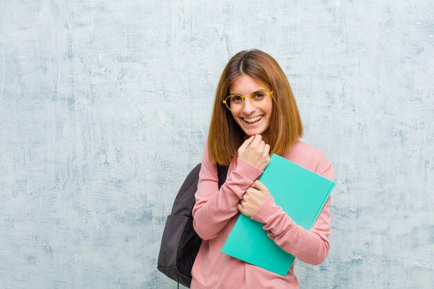 Jeune étudiante souriante, profitant de la vie, heureuse, amicale, satisfaite et insouciante avec la main sur le mur de menton grunge