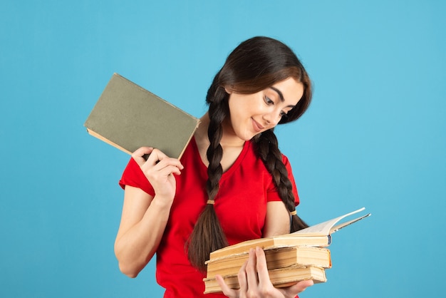 Jeune étudiante en t-shirt rouge lisant un nom de livre sur le mur bleu.