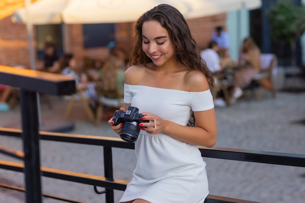 Jeune étudiante ou touriste séduisante utilisant un appareil photo sans miroir tout en marchant dans la ville d'été wo ...