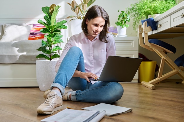 Jeune étudiante à l'université qui étudie à la maison assise sur le sol à l'aide d'un ordinateur portable