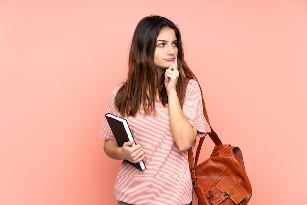 Jeune étudiante va à l'université sur rose isolé ayant des doutes et avec une expression de visage confuse