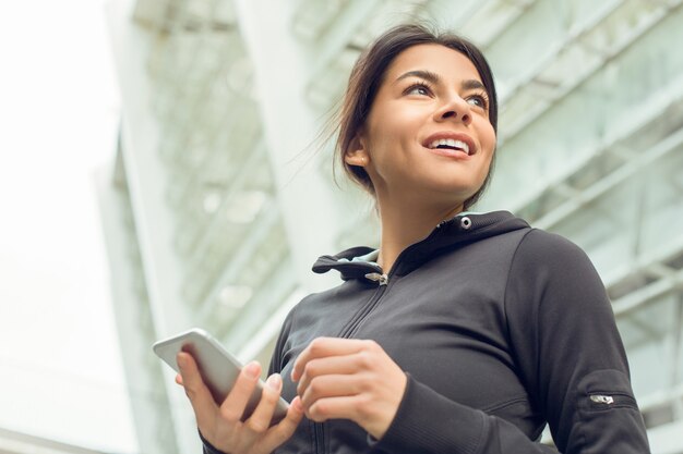 Jeune exercice d'exercice féminin dans la rue à l'extérieur à l'aide d'un smartphone