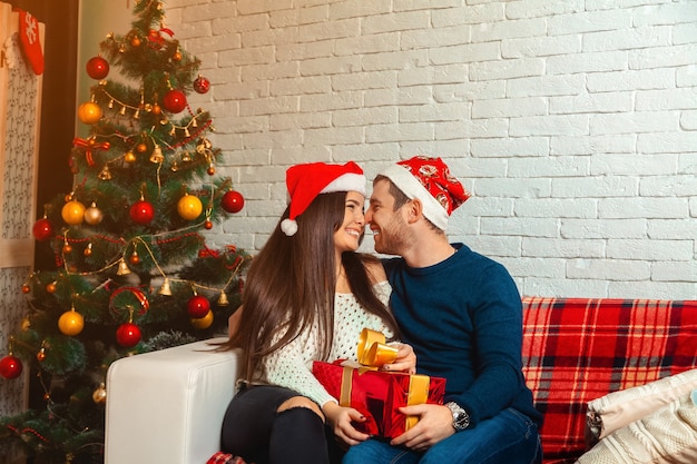 Une jeune famille amoureuse se regarde dans les yeux et rit la veille de Noël. Nouvelle année. Ambiance de Noël.