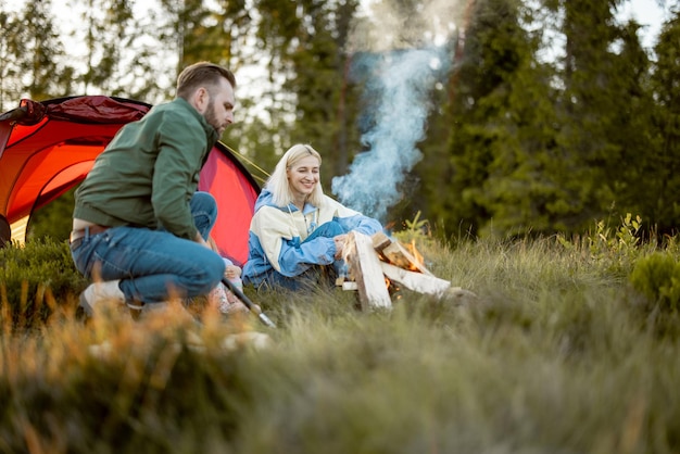 Jeune famille assise près du feu de camp près de la tente sur la nature