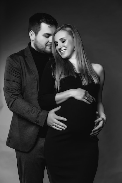 Une jeune famille attend la naissance d'un enfant. Le gars et la femme enceinte se tiennent l'un contre l'autre et se serrent sur un fond uni marron. Couple heureux aimant. Grossesse