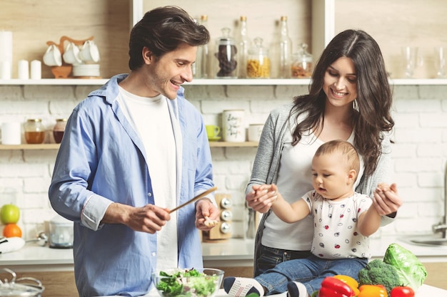 Jeune famille avec bébé préparant un déjeuner sain ensemble dans la cuisine