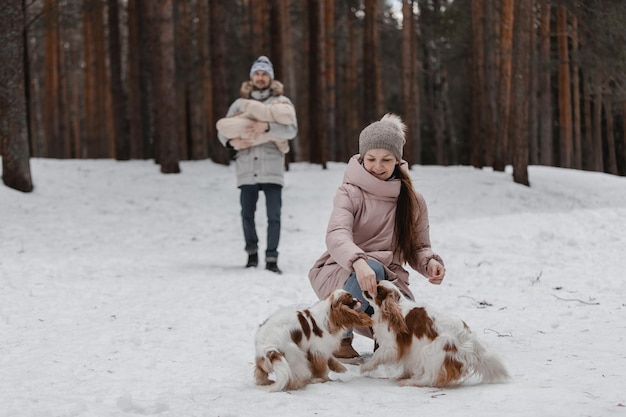 Une jeune famille caucasienne heureuse joue avec un chien en hiver dans une forêt de pins