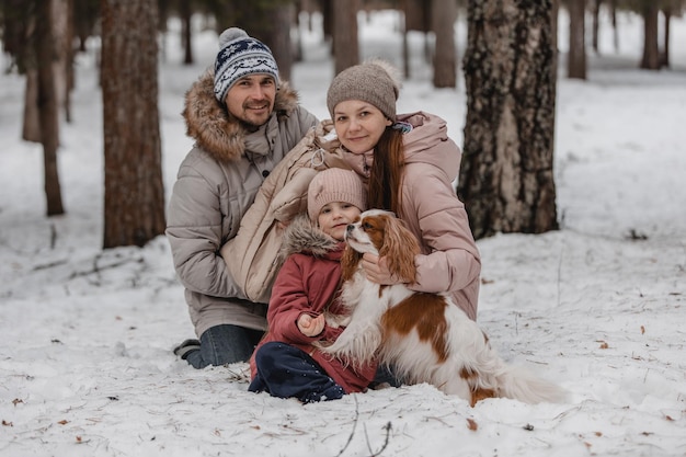 Une jeune famille caucasienne heureuse joue avec un chien en hiver dans une forêt de pins